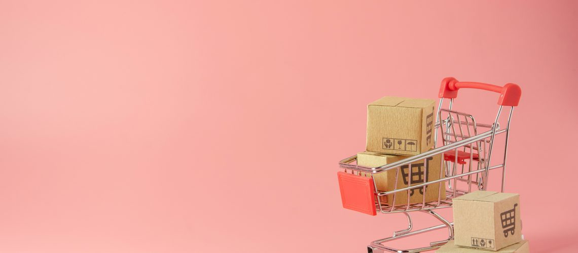 Image représentant des cartons dans un caddie de supermarché miniature. Sur un fond rose.